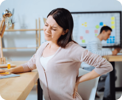 Woman standing at an office desk holding her lower back in pain