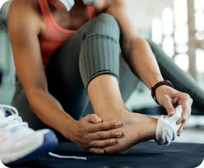 Person sitting on a gym floor holding their ankle in pain