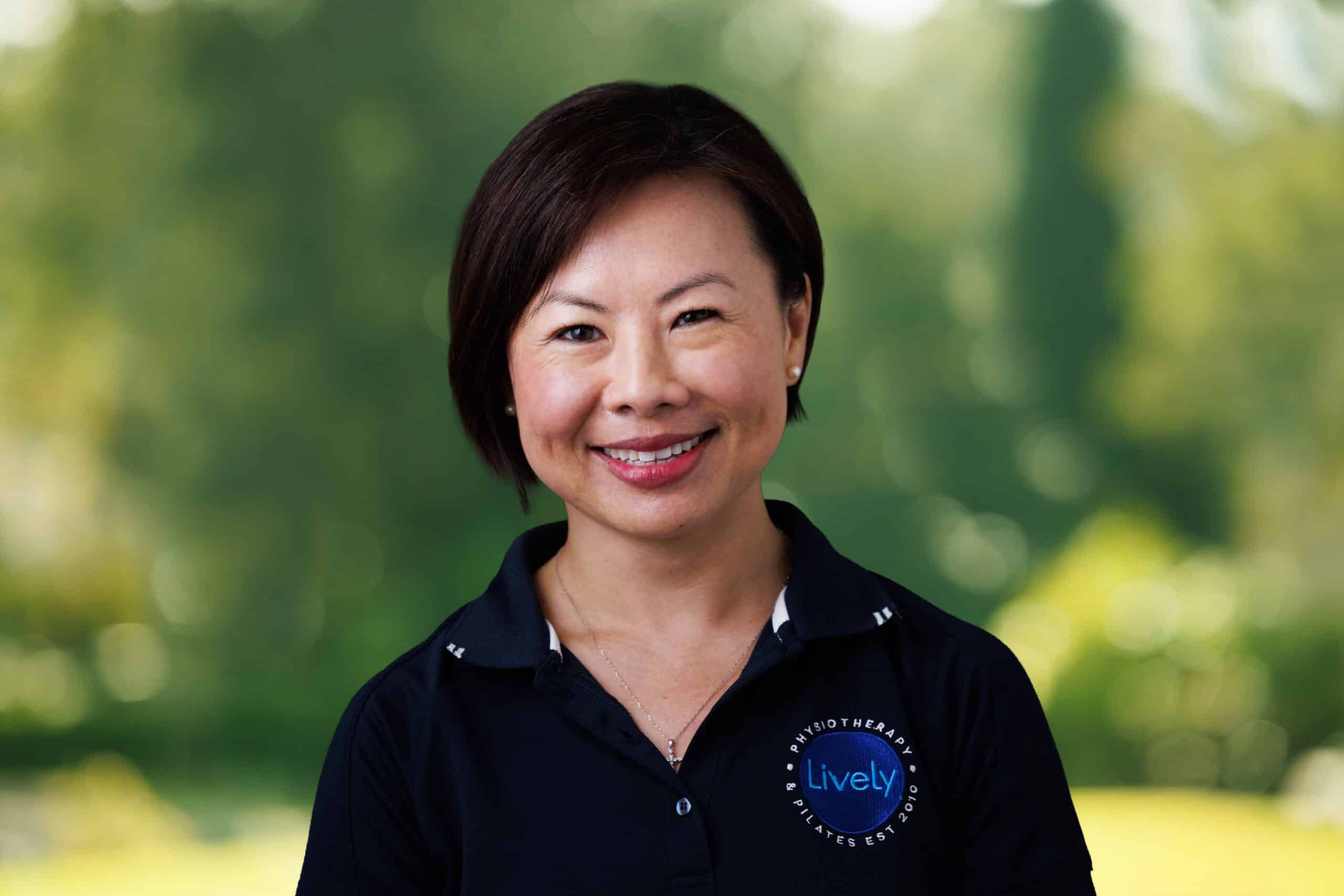 Sylvia Yong-Gonzales, team member at Lively Physio, smiling outdoors in a navy Lively Physio polo shirt