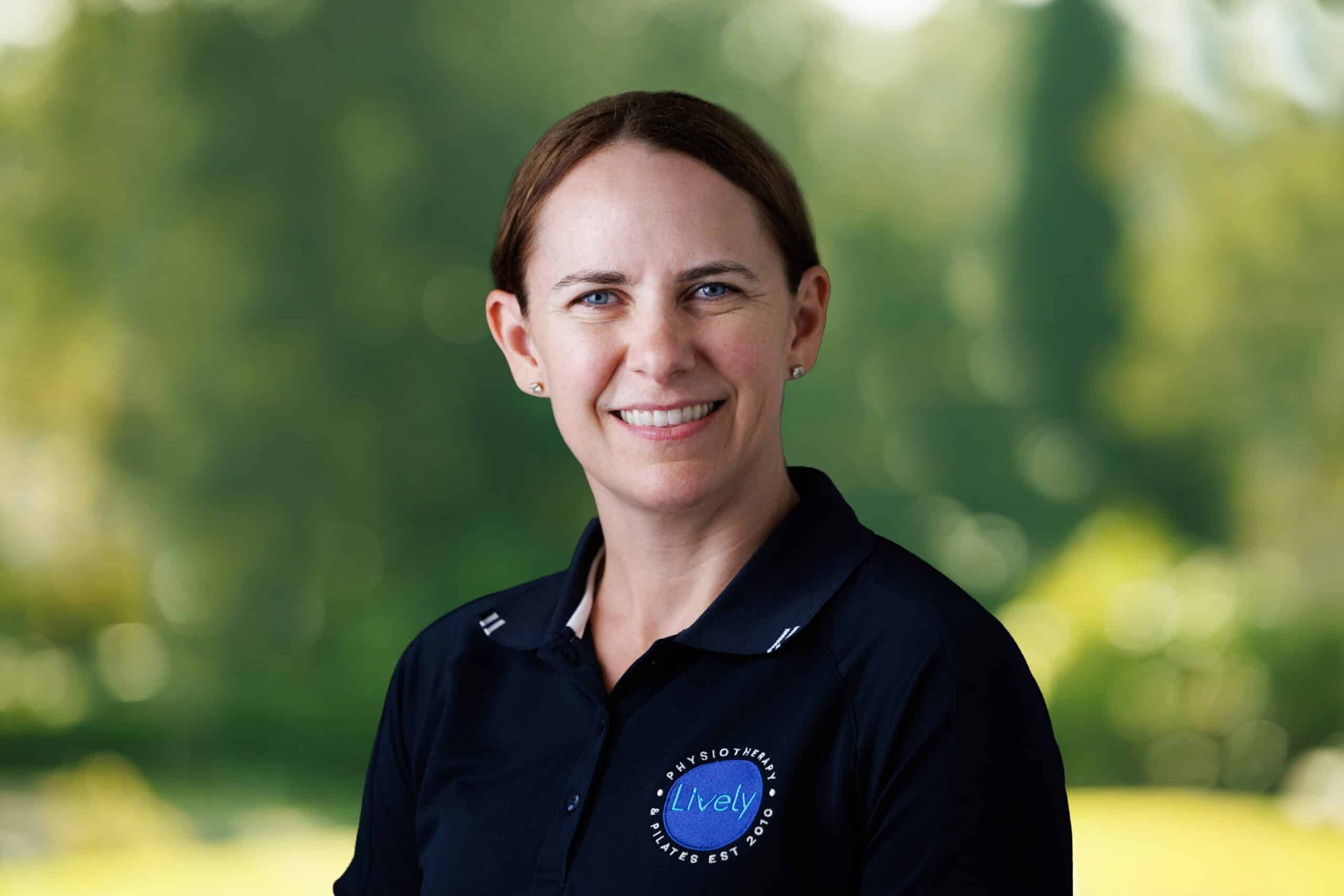 Christina Lorenz, team member at Lively Physio, smiling outdoors in a navy Lively Physio polo shirt