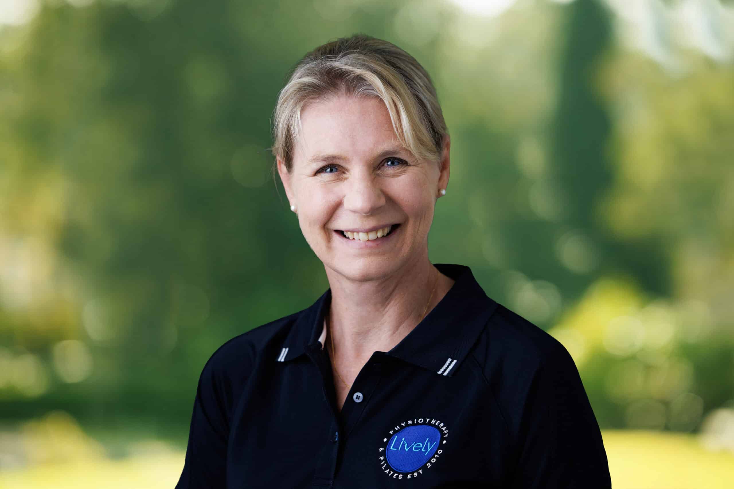 Christine Potter, team member at Lively Physio, smiling outdoors in a navy Lively Physio polo shirt