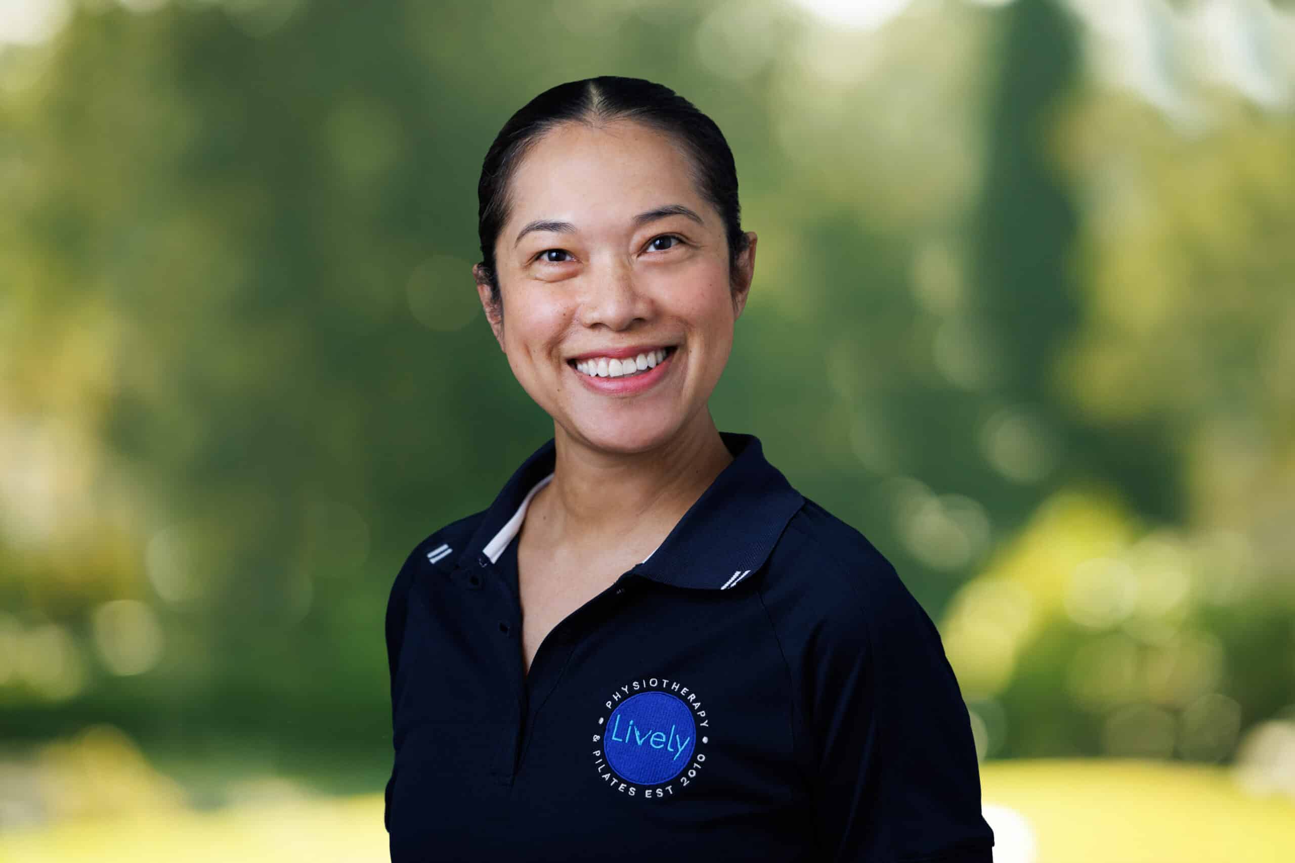 Oor Na Chiangmai, team member at Lively Physio, smiling outdoors in a navy Lively Physio polo shirt
