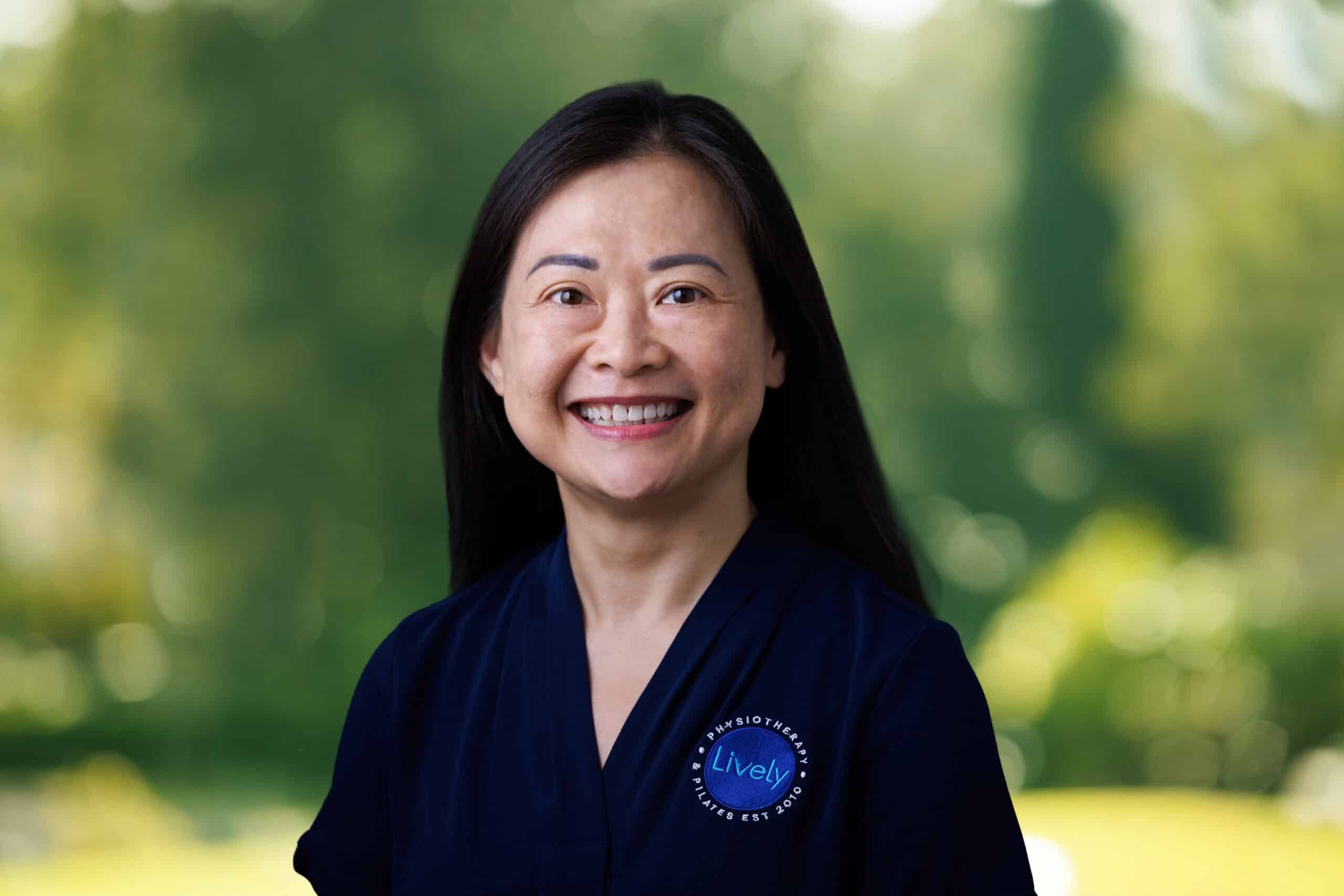 Fidi Yong, team member at Lively Physio, smiling outdoors in a navy Lively Physio polo shirt